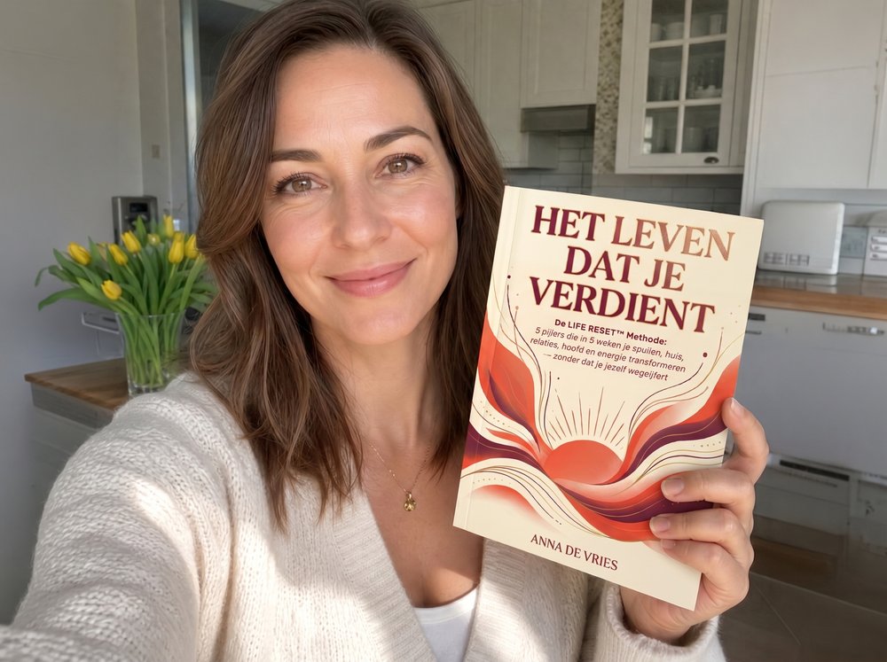 Lachende vrouw houdt het boek „Het Leven Dat Je Verdient” vast in de keuken bij een vaas tulpen